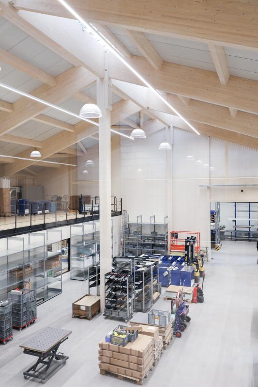 „Produktionshalle mit sichtbarer Holzkonstruktion, offener Galerieebene, hoher Raumstruktur und integrierter Linearbeleuchtung.“ geplant und umgesetzt von arc+